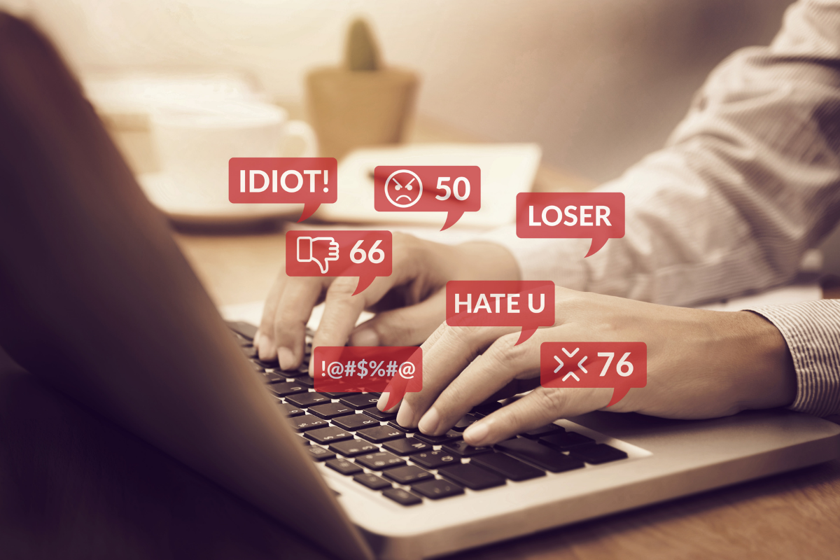 On the picture there is a keyboard and hands typing on it. There are red speech bubbles saying hurtful words like "IDIOT", "LOSER" and "HATE YOU"