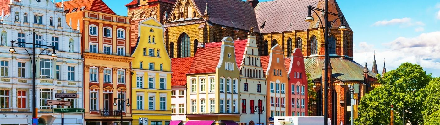 Auf dem Foto ist eine deutsche Stadt zu sehen. Die Häuser sind bunt und im Hintergrund ist eine Kirche zu sehen. Der Himmel ist blau und die Sonne scheint.