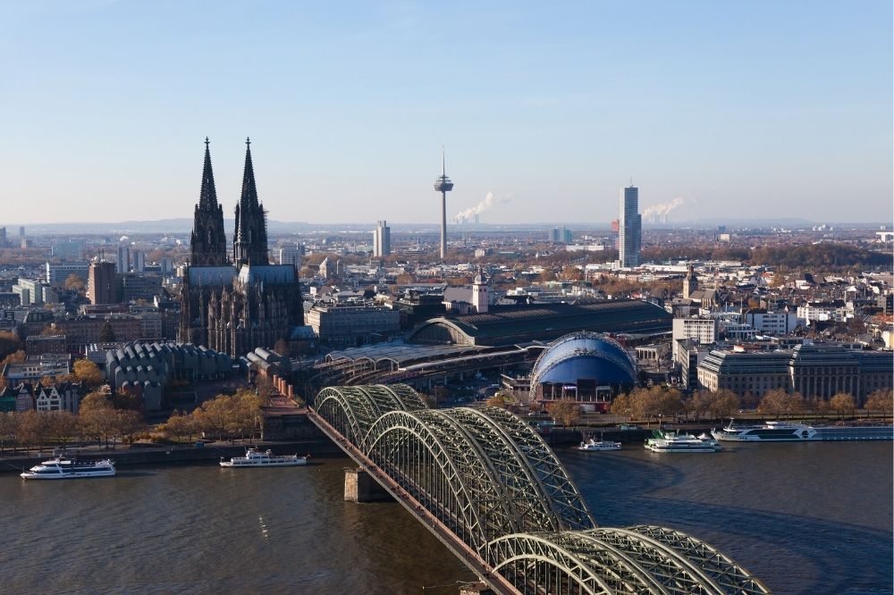 Auf dem Bild sieht man Köln aus der Vogelperspektive fotografiert. Im hinteren Bildrand links ist der kölner Dom zu erkennen. Ebenso sieht man den Rhein sowie die Hohenzollernbrücke.