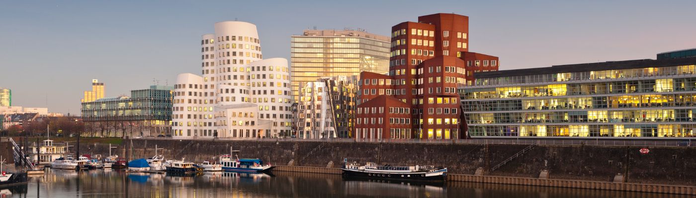 Auf dem Foto ist Düsseldorf zu sehen. Vorne links im Bild ist ein Fluss zu sehen. Rechts im Bild sind Häuser zu sehen, die an das Wasser gebaut wurden.