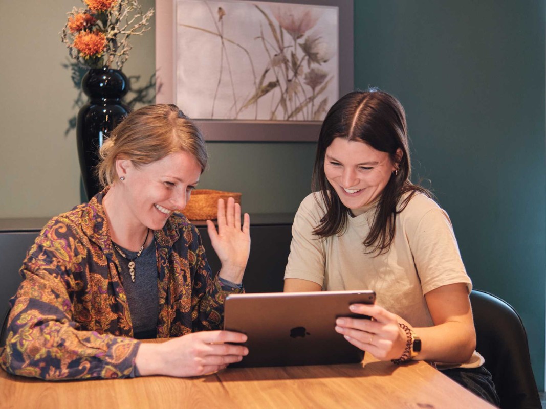 Zwei Personen engagieren sich im Mini-Engagement für Little World, sitzen zusammen am Tisch und lachen in ein Tablet.