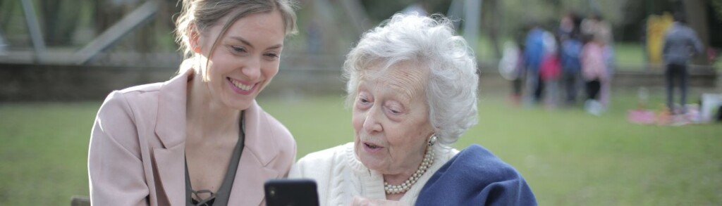 Ehrenamtliche Betreuerin und Seniorin schauen sich zusammen etwas auf dem Handy an.