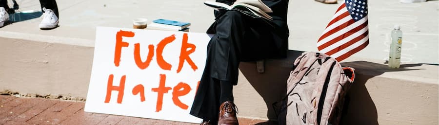 Ein Mann sitzt auf einer Mauer und neben ihm steht ein Schild mit "Fuck Hate